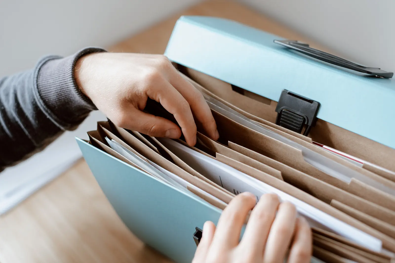 Hands sorting documents in a blue expanding file as an illustration of audit-ready record keeping