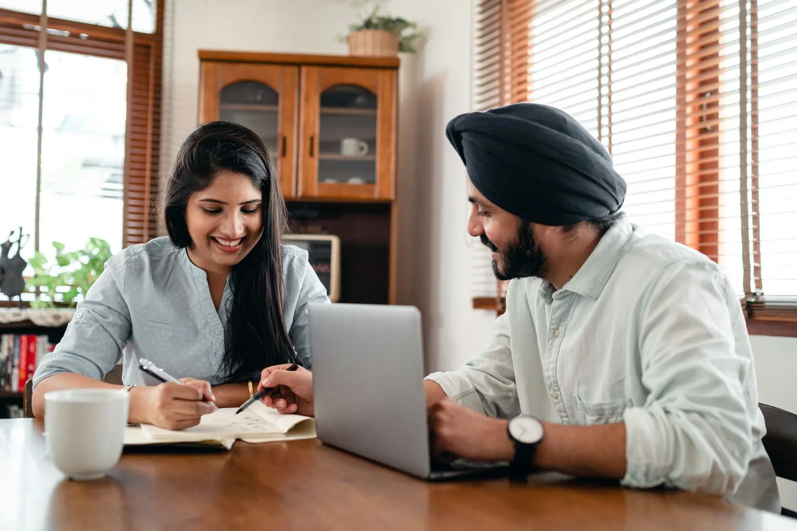Two Indian colleagues discussing notes together beside a laptop in a bright workspace