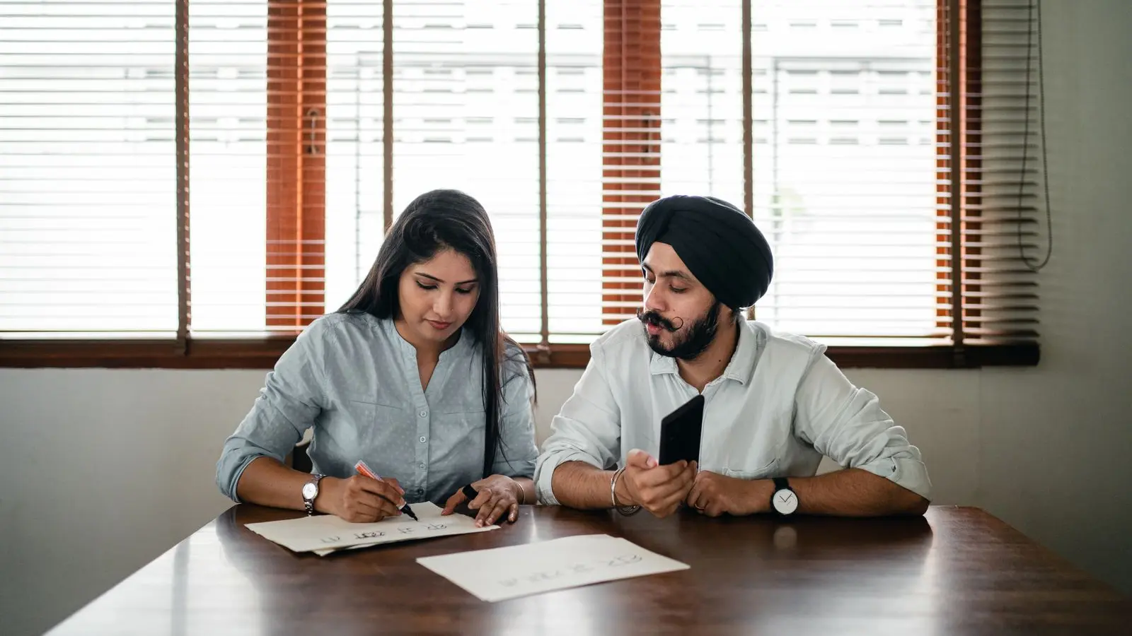 Two Indian colleagues reviewing papers and writing notes together at a table
