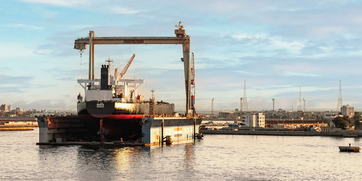 A ship in a floating dry dock beneath a large gantry crane in Suez, Egypt.